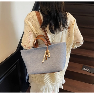 Close-up of light blue denim tote bag with brown leather handles and bead charm detail
