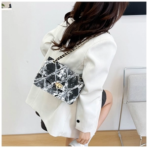 Détail du sac matelassé en denim gris foncé avec chaîne dorée sur un blazer blanc chic