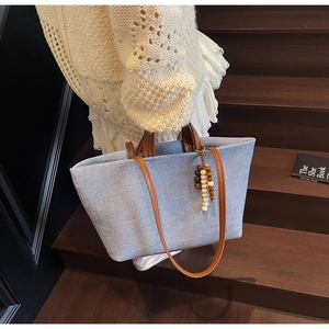 Detail of light blue denim tote bag with brown leather handles and beaded charm