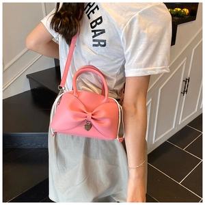 Detail of pink bow-shaped handbag with heart pendant shown in a lifestyle street style