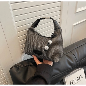 Detail of woven texture handbag featuring elegant pearl charms and black leather handle