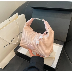 Detail of pink woven handbag with leather handle and decorative bead charm against a gift box
