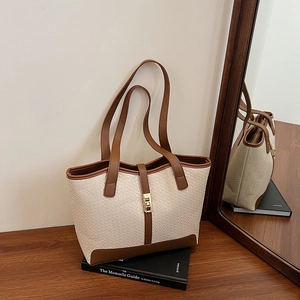 Chic cream woven tote bag with brown handles and gold buckle on a minimalist desk