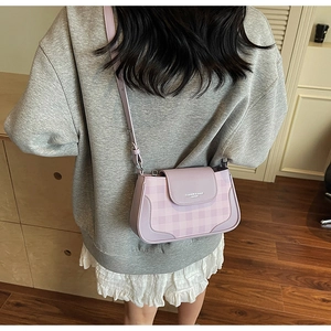 Detail of lavender plaid crossbody bag with leather patch on a model in home setting