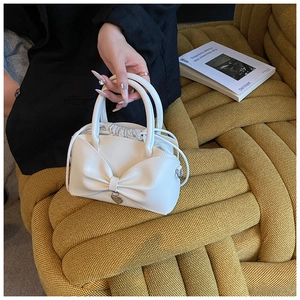 Detail of white bow handbag with heart charm and drawstring closure on woven background