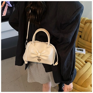 Close-up of cream bow shoulder bag with heart pendant worn in a cozy lifestyle setting