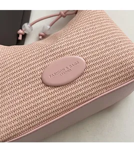 Close-up of pink woven handbag featuring leather patch detail and decorative beads