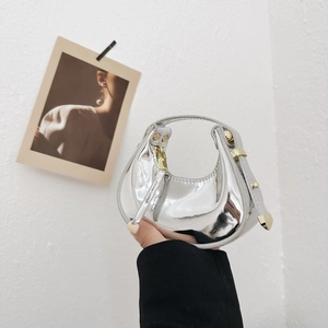 Metallic silver crescent mini handbag with gold zipper held against a white wall background