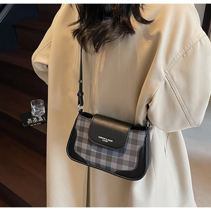 Detail of grey plaid crossbody bag with black leather flap and adjustable strap on a model