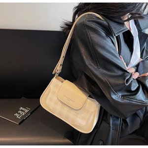 Detail view of a cream checkered underarm bag with an adjustable strap worn by a model