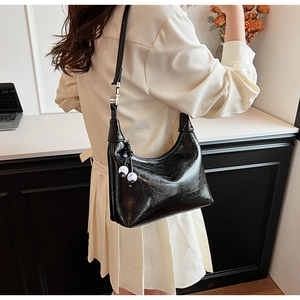 Détail du sac hobo noir en cuir plissé brillant avec pendentifs boules et bandoulière