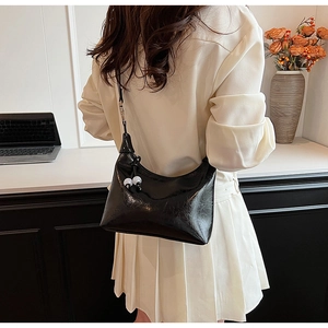Détail du sac à bandoulière noir brillant avec une élégante breloque en perles bicolores