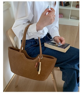 Brown woven tote bag with beaded tassel charm held by model in a cozy casual lifestyle setting