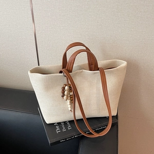 Large canvas tote bag with brown leather straps and beaded tassel on art book background