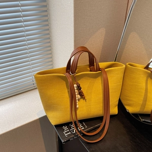 Large yellow canvas tote bag with leather straps and decorative beads on a black surface