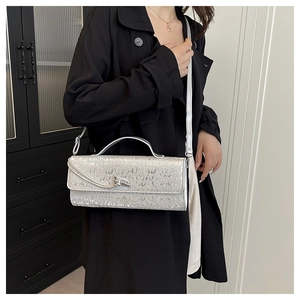 Borsa baguette glitterata argento indossata con un cappotto nero per un look elegante