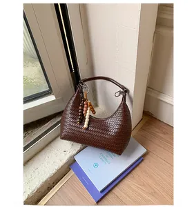 Gros plan du sac tressé marron foncé avec texture cuir et pompon en perles de bois