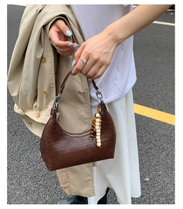 Close-up of a woven dark brown leather hobo bag featuring a bohemian beaded tassel detail