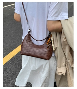Detail of dark brown woven crescent bag with wood bead charm and metallic zipper