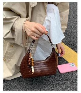Detail of dark brown woven crescent bag with colorful wooden bead charm and metal zipper