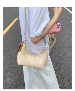 Close-up of beige woven hobo bag with wooden bead charm detail in outdoor street setting