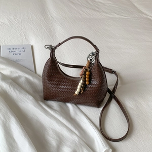Grand sac hobo tressé marron foncé avec perles en bois sur fond en tissu blanc