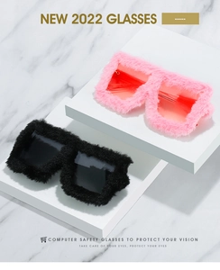 Detail of plush cat eye sunglasses with furry frames in pink and black displayed on marble