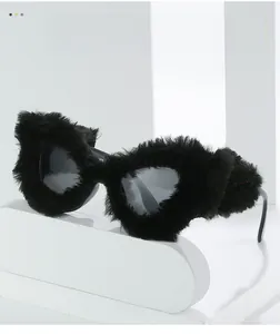 Detailaufnahme einer Katzenaugen-Sonnenbrille mit dichtem schwarzem Plüschbesatz auf weißem Sockel