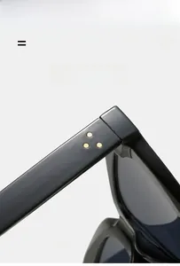 Detail einer schwarzen quadratischen Sonnenbrille mit drei goldenen Nieten am Bügel