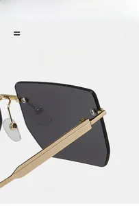 Detail view of gold metal temples and gradient grey lenses on rimless square sunglasses