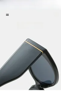 Detail view of oval sunglasses featuring black frames and gold metal hinge accents