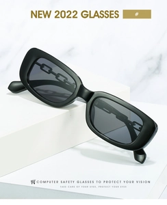 Détail de lunettes de soleil carrées noires avec branches en chaîne sur marbre