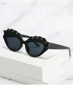 Détail de lunettes de soleil œil-de-chat noires avec bords ondulés sur socle blanc