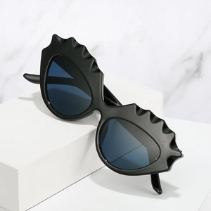 Lunettes de soleil œil de chat avant-garde avec monture noire ondulée sur socle blanc