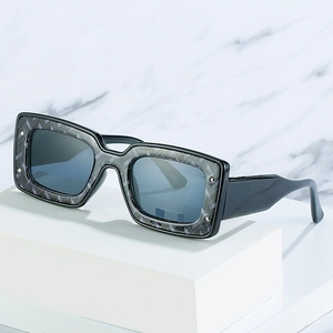 Quadratische schwarze Sonnenbrille mit grauen Mustern und Nieten auf weißem Marmorsockel