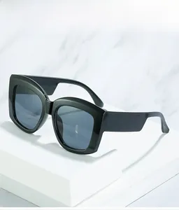 Detail of oversized black sunglasses with wide temples on a minimalist marble display