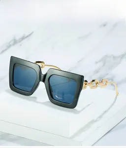 Detail of square oversized sunglasses with gold metal chain temple design on marble