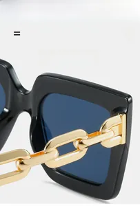 Detail of square oversized sunglasses featuring gold chain temples and blue lenses