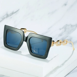 Chic oversized square sunglasses with gold chain temples and blue lenses on a marble stand