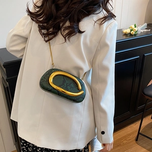 Detail of dark green snake texture bag with bold golden buckle and chain strap