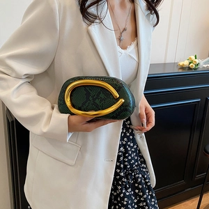 Detail showing dark green snakeskin texture and golden C-shaped handle of the fashion bag