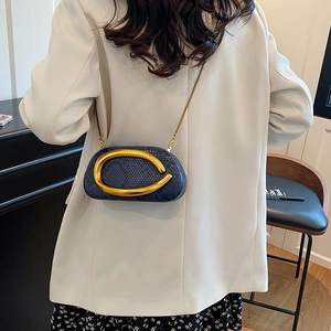 Detail of dark blue python textured chain bag with large gold ring on white blazer