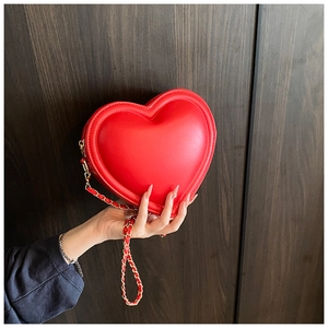 Close-up of red heart-shaped leather bag with gold chain strap and fine stitching details