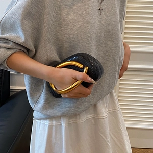 Detail showing snake pattern leather and bold gold U-shaped handle on a black evening bag