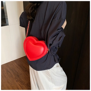 Detail of red heart-shaped crossbody bag with gold chain strap on a model back