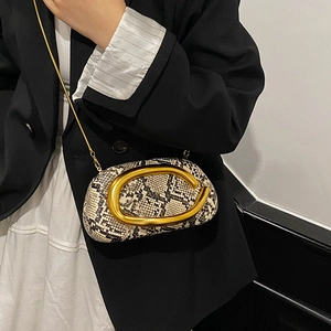 Detail of snake pattern crossbody bag with large golden C-shaped metal buckle on the front