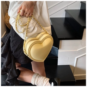 Detail of a creamy yellow heart-shaped crossbody bag with woven gold chain and dual zippers