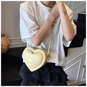 Close-up of cream heart-shaped crossbody bag with gold chain strap on model