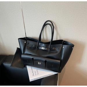 Detail of a large black leather tote bag featuring a classic flap lock and front pocket