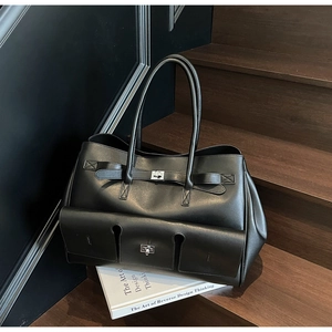 Detail of black multi-pocket tote bag with silver twist locks on wooden stairs